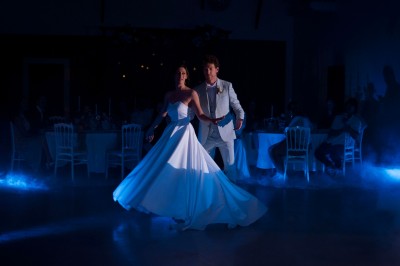 Une mariée en robe blanche tient un bouquet coloré face à un homme en costume clair dans un jardin verdoyant.