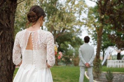 Une mariée en robe blanche tient un bouquet coloré face à un homme en costume clair dans un jardin verdoyant.
