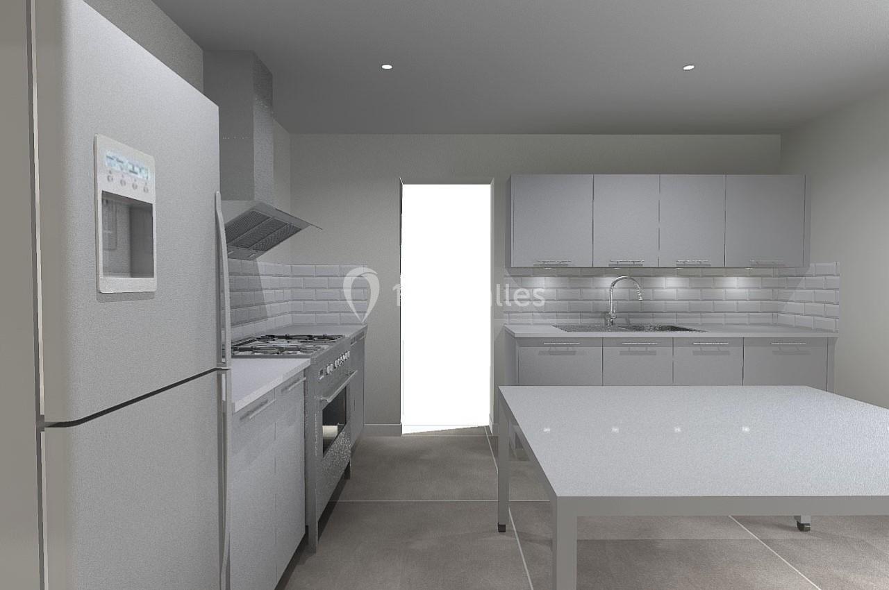 Cuisine moderne avec réfrigérateur, cuisinière, évier et table, éclairée par une lumière naturelle provenant d'une porte.