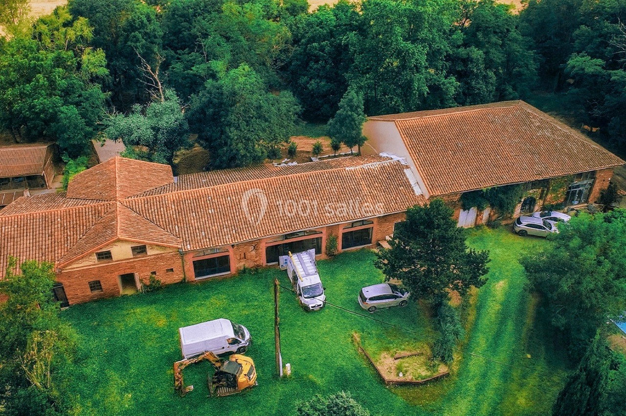 Vue aérienne d'un grand bâtiment en briques rouges entouré d'arbres, avec des véhicules stationnés sur la pelouse.