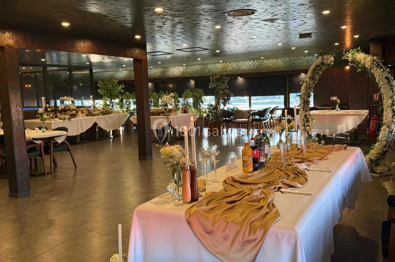 Salle de réception décorée avec des tables dressées, des chandeliers et un arc floral, ambiance élégante et lumineuse.