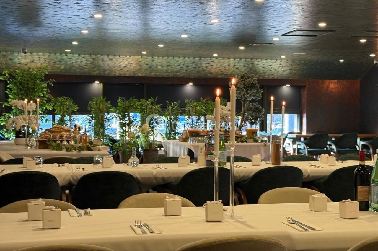 Salle de réception décorée avec des tables dressées, chandeliers allumés et plantes en arrière-plan.