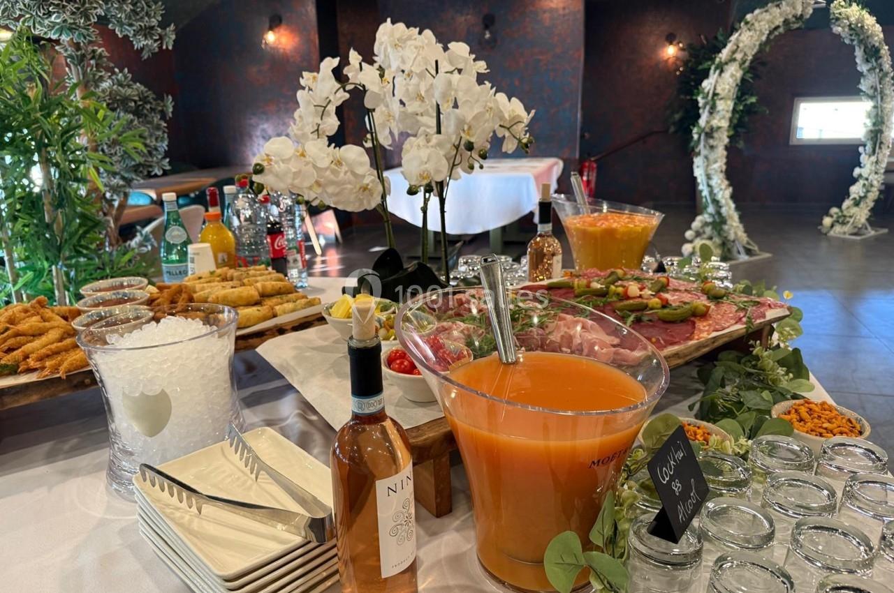 Buffet avec boissons, charcuterie, légumes, fleurs blanches et décorations pour un événement festif en intérieur.