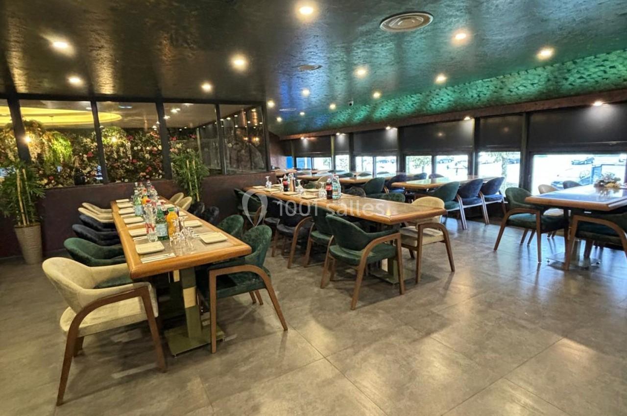 Salle de restaurant moderne avec tables en bois, chaises rembourrées et décoration végétale sur les murs.