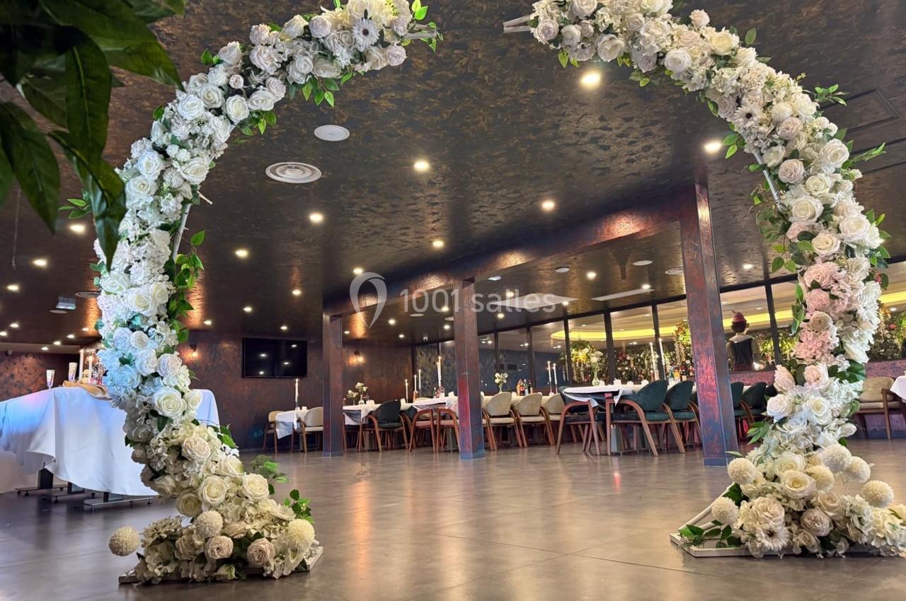 Arche circulaire décorée de fleurs blanches dans une salle de réception élégante avec tables dressées en arrière-plan.
