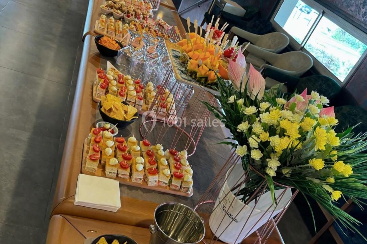 Buffet composé de canapés, brochettes de fruits, chips et fleurs décoratives sur une table en intérieur.