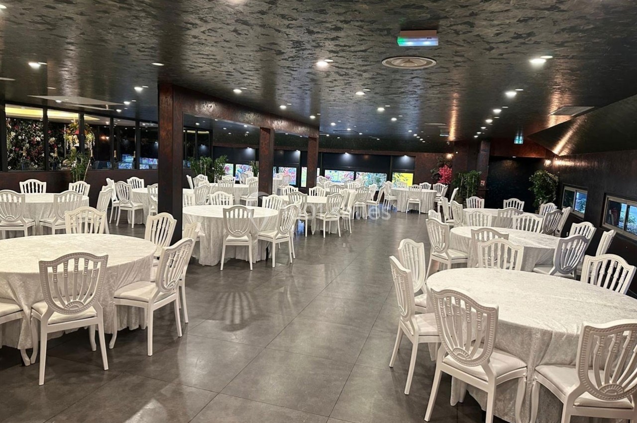 Salle de réception spacieuse avec tables rondes dressées de nappes blanches et chaises blanches, éclairage tamisé.