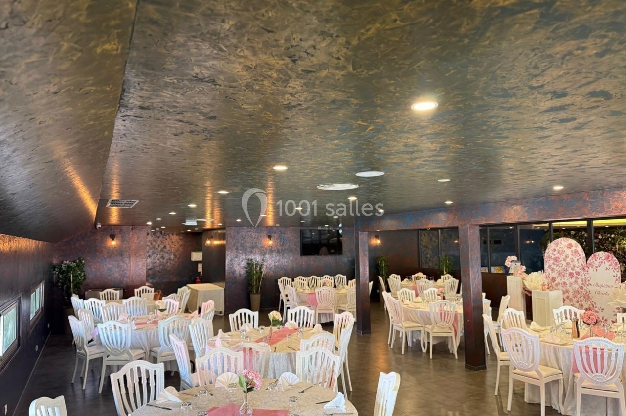 Salle de réception décorée avec des tables rondes dressées, chaises blanches et ambiance lumineuse.