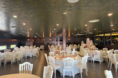 Salle de réception décorée avec des tables rondes dressées, chaises blanches et ambiance lumineuse chaleureuse.