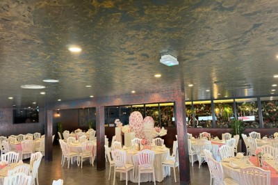Salle de réception décorée avec des tables rondes dressées, chaises blanches et ambiance lumineuse chaleureuse.