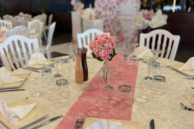 Salle de réception décorée avec des tables rondes dressées, chaises blanches et ambiance lumineuse chaleureuse.