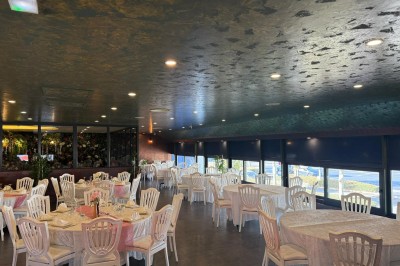 Salle de réception décorée avec des tables rondes dressées, chaises blanches et ambiance lumineuse chaleureuse.