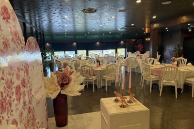 Salle de réception décorée avec des tables rondes dressées, chaises blanches et ambiance lumineuse chaleureuse.