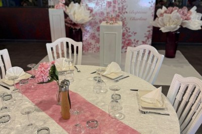 Salle de réception décorée avec des tables rondes dressées, chaises blanches et ambiance lumineuse chaleureuse.
