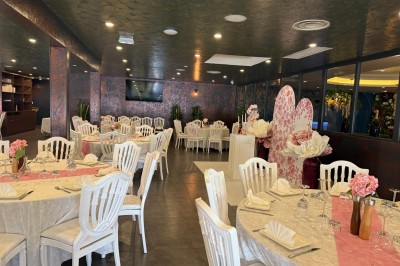 Salle de réception décorée avec des tables rondes dressées, chaises blanches et ambiance lumineuse chaleureuse.