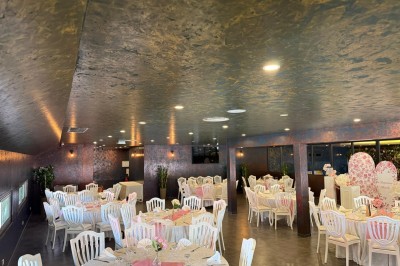 Salle de réception décorée avec des tables rondes dressées, chaises blanches et ambiance lumineuse chaleureuse.