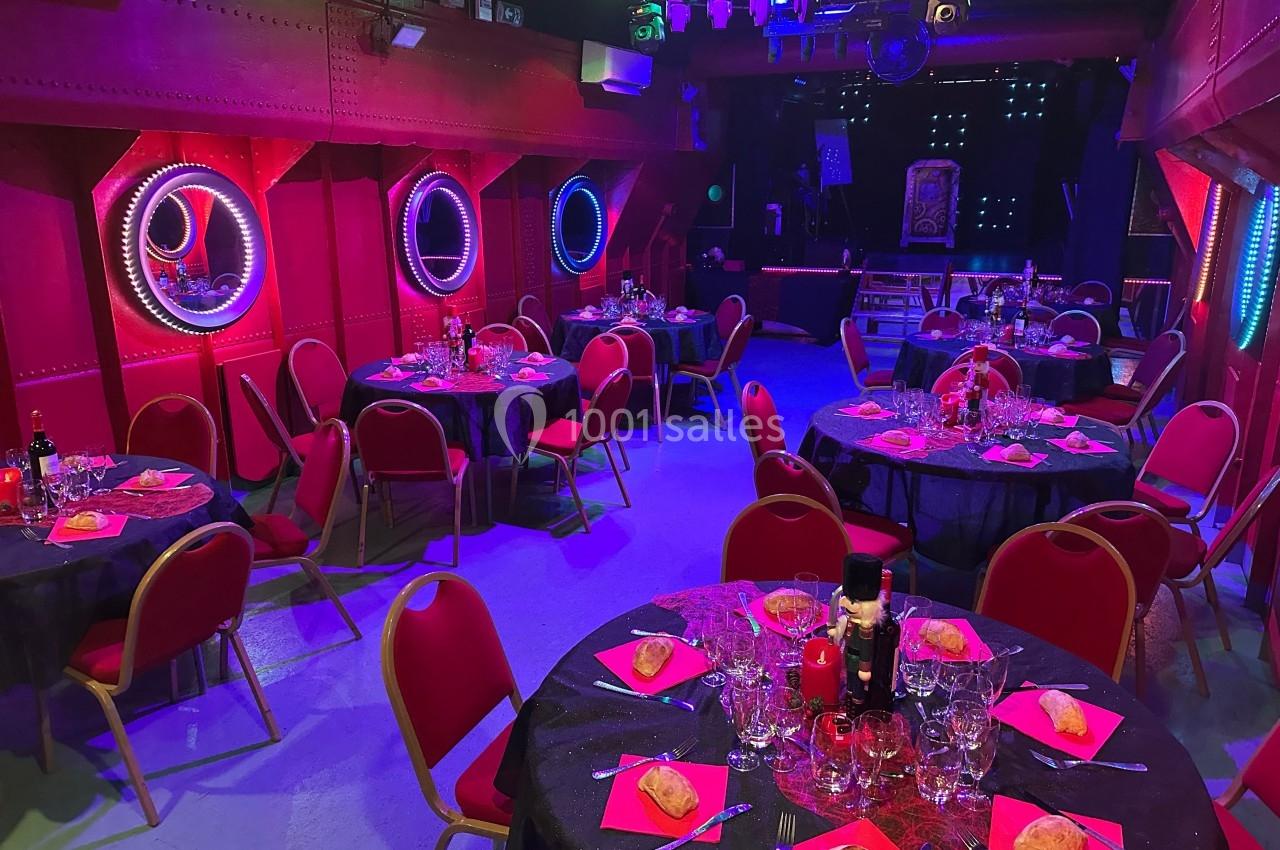 Salle décorée avec des tables rondes dressées pour un repas, éclairage coloré et ambiance festive.