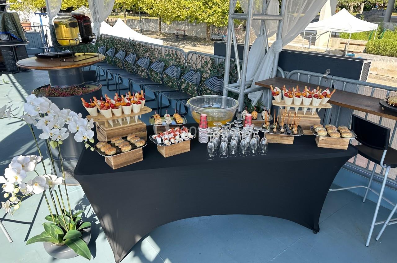 Table de buffet avec desserts variés, fruits frais, verrines et fleurs blanches en décoration, en extérieur.