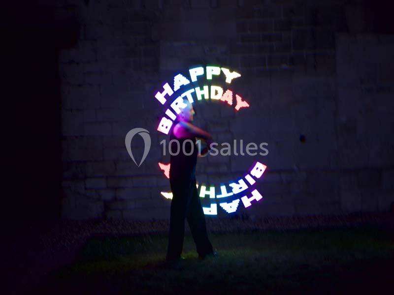 Personne jonglant avec des objets lumineux formant les mots ’Happy Birthday’ dans un espace extérieur sombre.