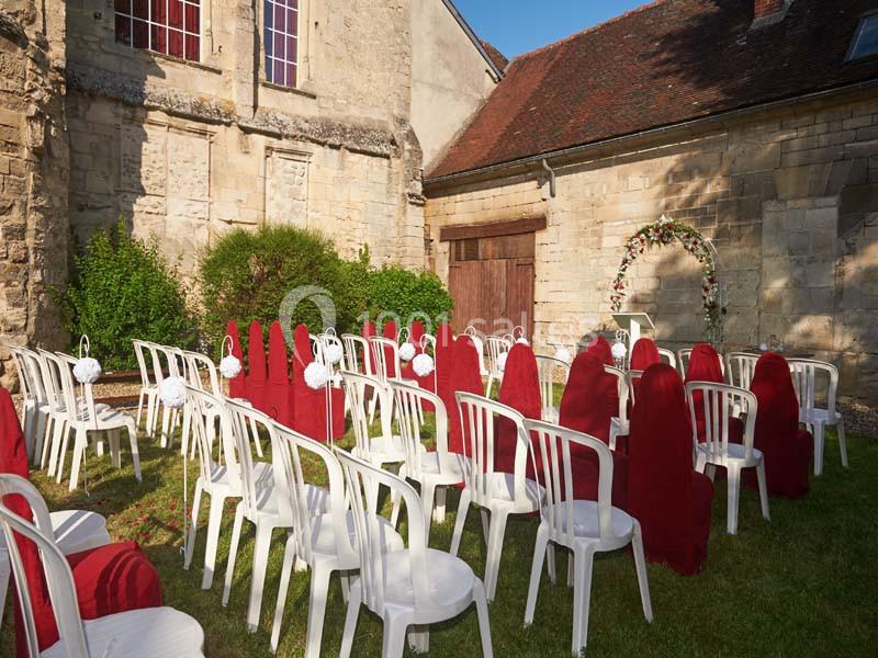 Chaises blanches et housses rouges disposées en extérieur pour une cérémonie devant un bâtiment en pierre.