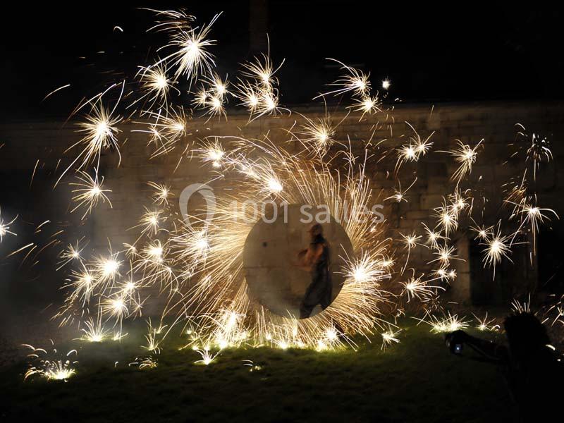 Personne marchant à travers un cercle métallique entouré d'étincelles lumineuses dans un environnement nocturne.