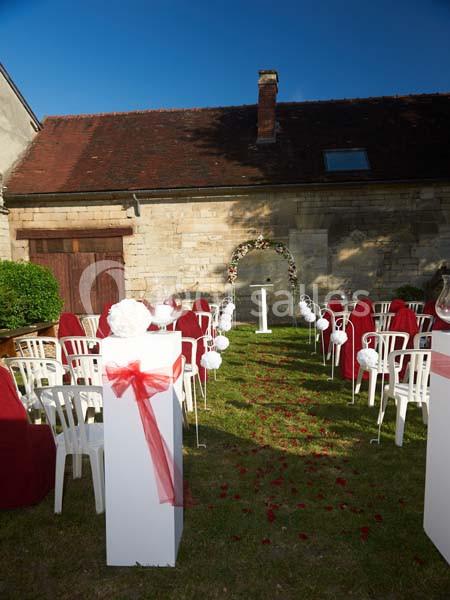 Chaises blanches et rouges disposées en extérieur pour une cérémonie, avec une arche fleurie en arrière-plan.