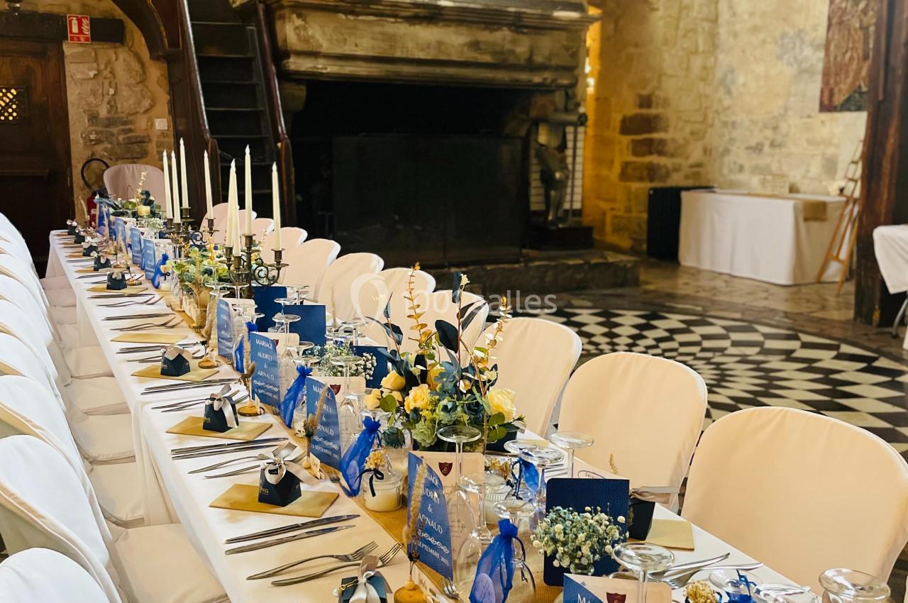 Table de banquet décorée avec des fleurs, des bougies et des cadeaux, dans une salle en pierre au style médiéval.