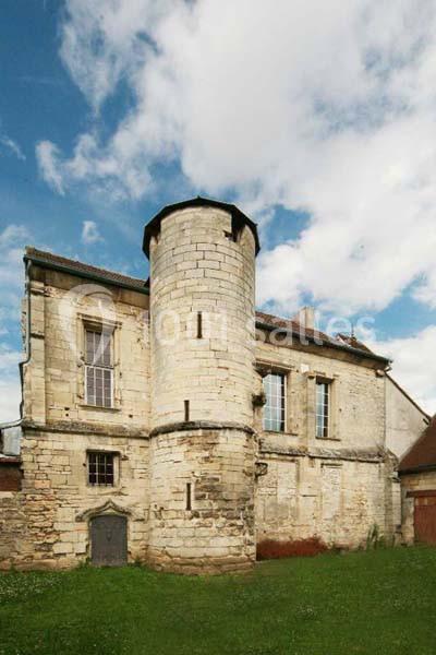 Bâtiment en pierre ancienne avec une tour cylindrique, fenêtres à croisillons et toit en pente sous un ciel partiellement…