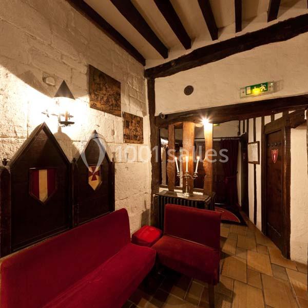 Intérieur rustique avec murs en pierre, poutres apparentes, bancs rouges et éclairage chaleureux.