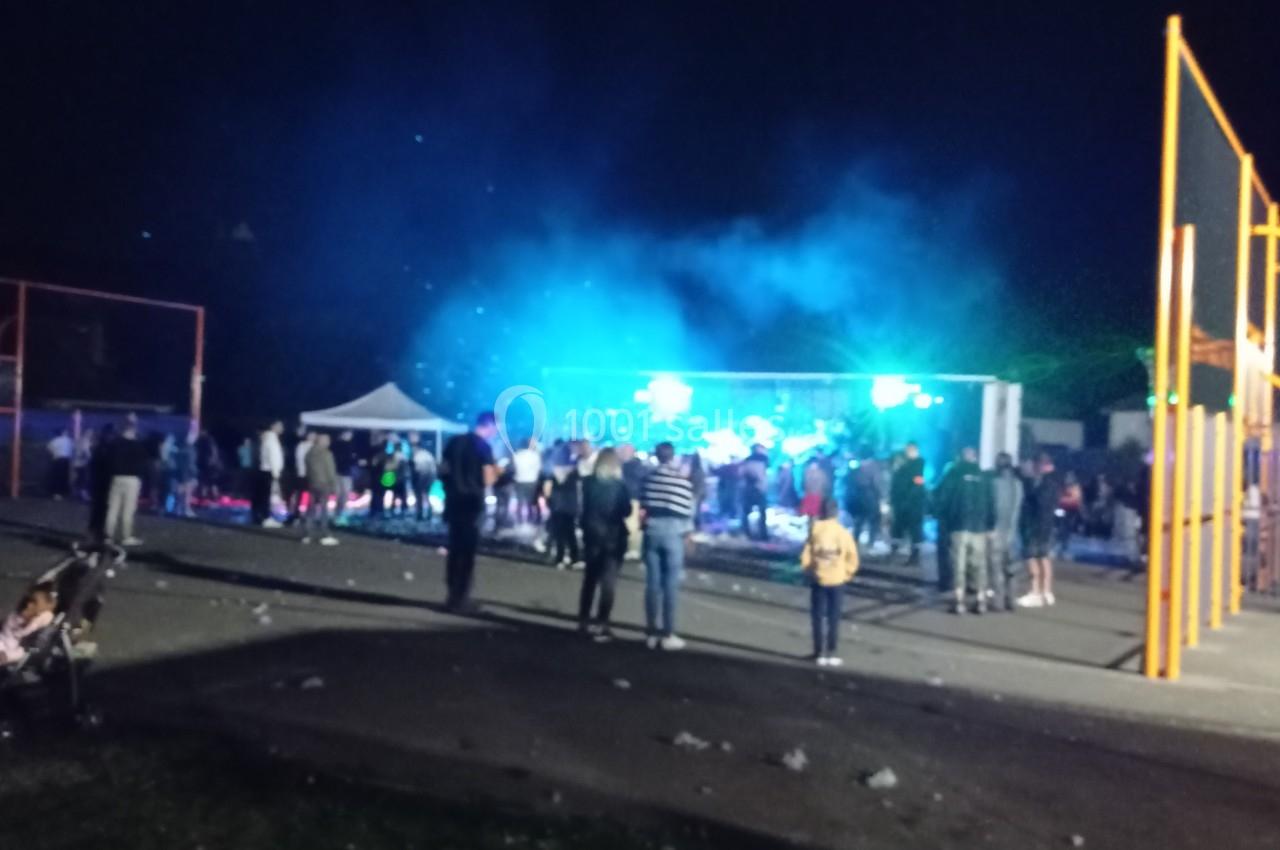 Groupe de personnes rassemblées en soirée devant une scène éclairée par des lumières colorées en extérieur.