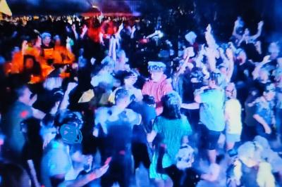 Foule dansante lors d'un événement nocturne en extérieur, éclairée par des lumières colorées.
