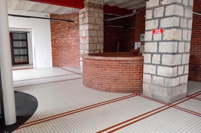 Espace intérieur avec murs en briques et pierres, sol carrelé blanc à motifs rouges, et comptoir circulaire en briques.