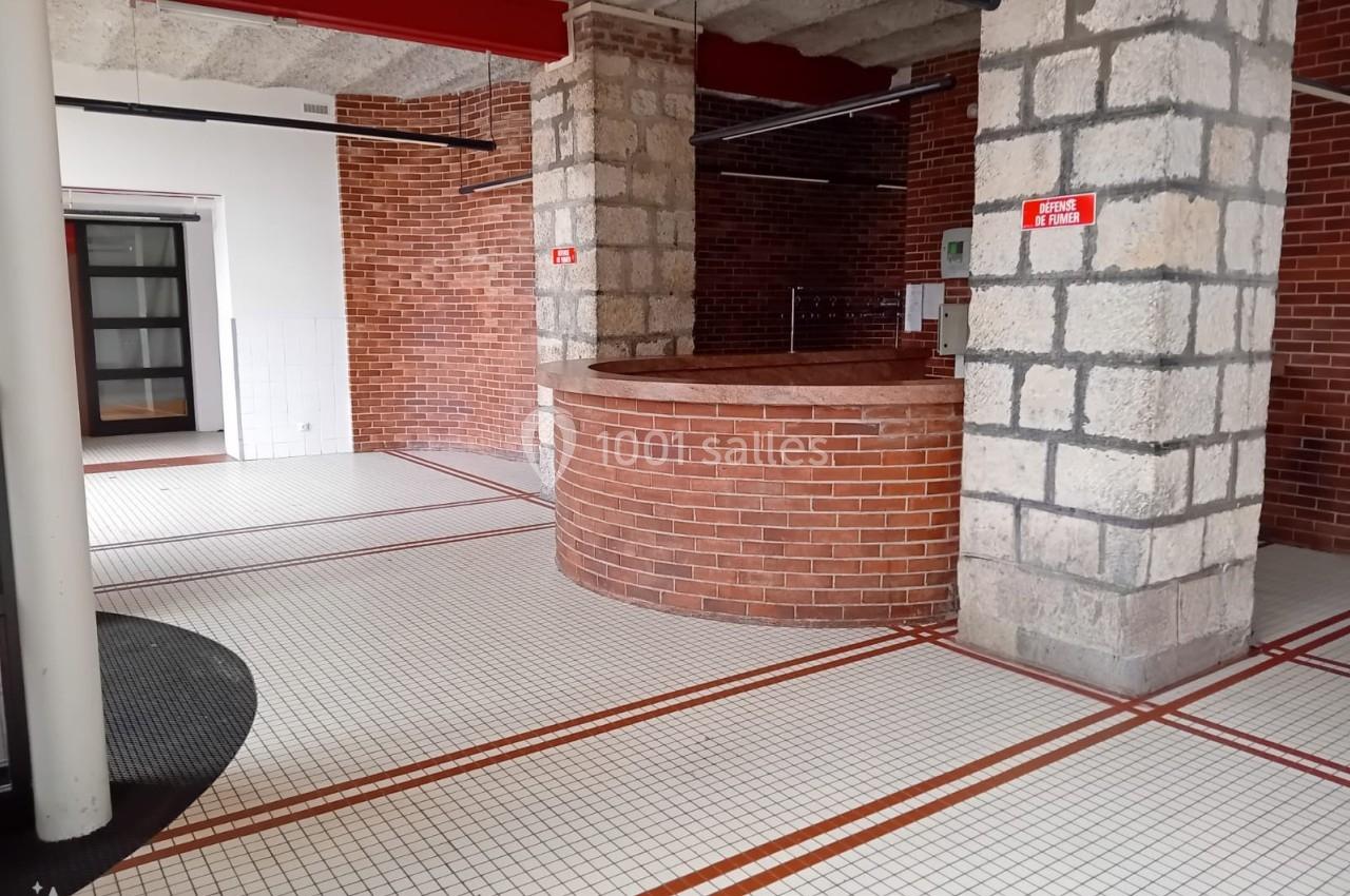 Espace intérieur avec murs en briques et pierres, sol carrelé blanc à motifs rouges, et comptoir circulaire en briques.