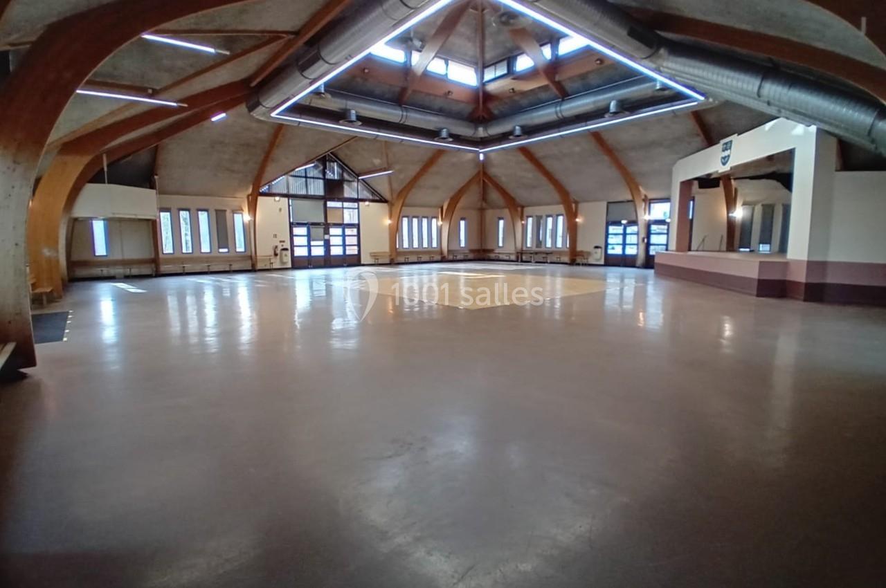 Salle spacieuse avec charpente en bois apparente, grandes fenêtres et sol en béton poli.