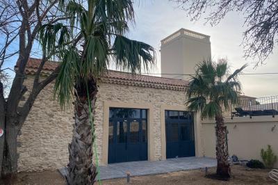 Terrasse en pierre avec piscine, chaises longues, parasols et bâtiments en pierre sous un ciel dégagé.