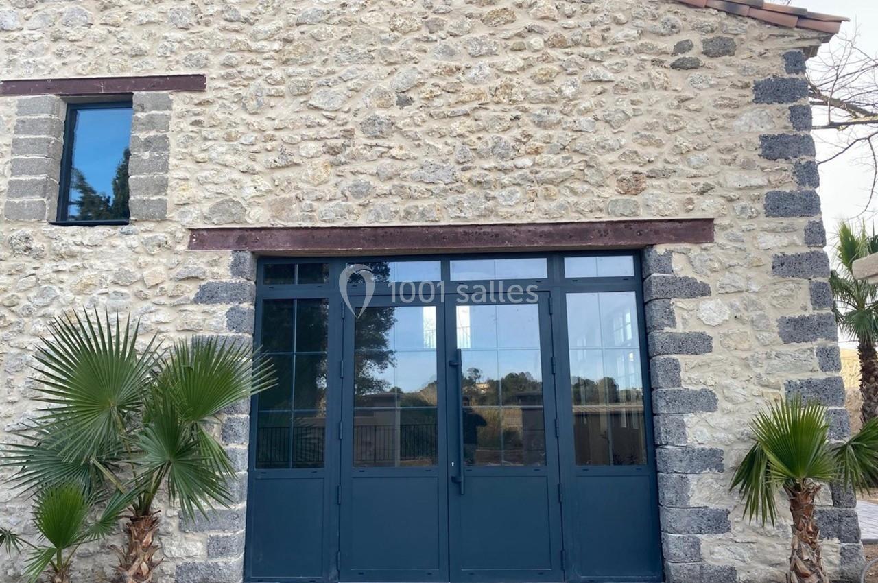 Façade en pierre avec une grande porte vitrée noire et des palmiers plantés devant.