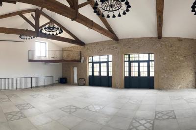 Terrasse en pierre avec piscine, chaises longues, parasols et bâtiments en pierre sous un ciel dégagé.