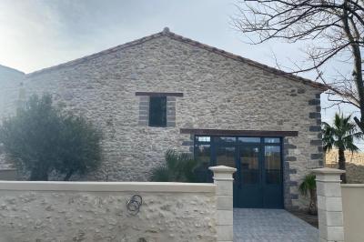 Terrasse en pierre avec piscine, chaises longues, parasols et bâtiments en pierre sous un ciel dégagé.