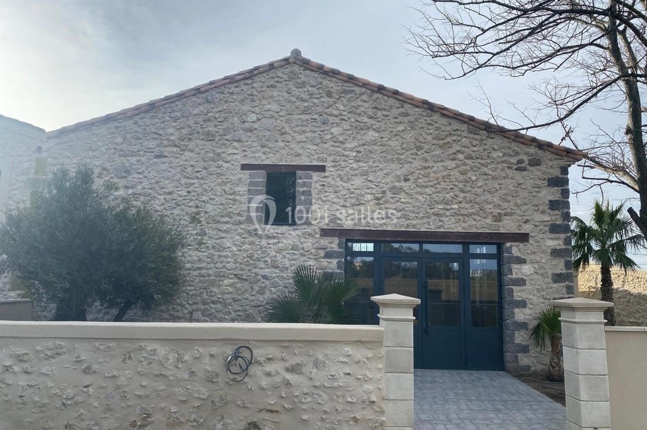 Façade d'une maison en pierre avec toit en tuiles, grande porte vitrée et mur d'enceinte en pierre.
