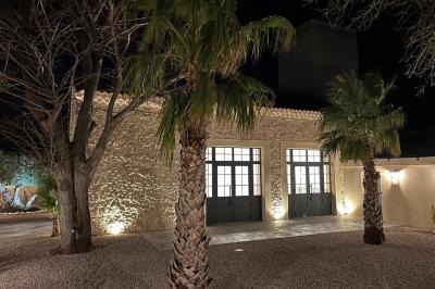 Terrasse en pierre avec piscine, chaises longues, parasols et bâtiments en pierre sous un ciel dégagé.