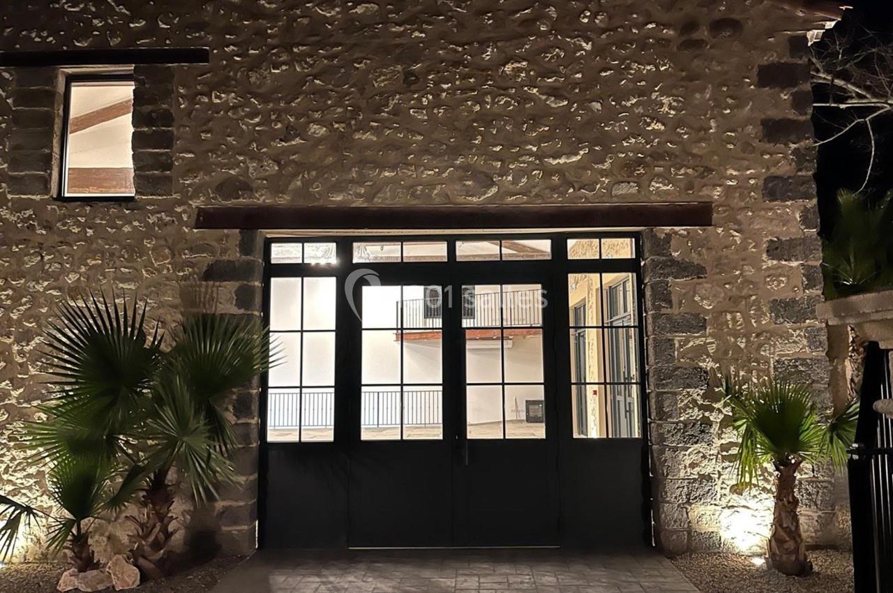 Façade en pierre avec une grande porte vitrée noire, éclairée par des lumières extérieures la nuit.