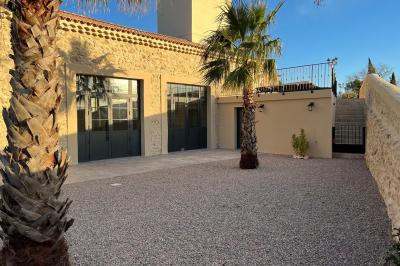 Terrasse en pierre avec piscine, chaises longues, parasols et bâtiments en pierre sous un ciel dégagé.