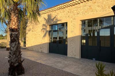 Terrasse en pierre avec piscine, chaises longues, parasols et bâtiments en pierre sous un ciel dégagé.