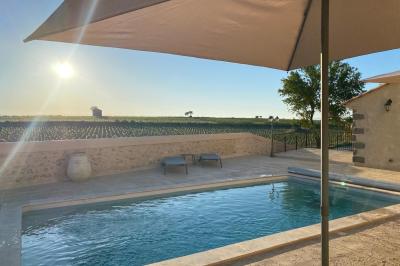 Terrasse en pierre avec piscine, chaises longues, parasols et bâtiments en pierre sous un ciel dégagé.