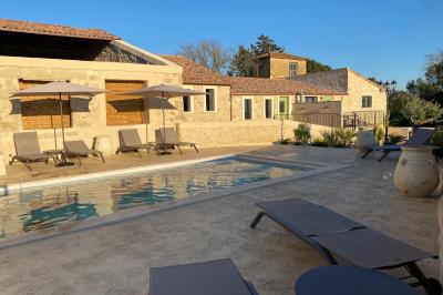 Terrasse en pierre avec piscine, chaises longues, parasols et bâtiments en pierre sous un ciel dégagé.
