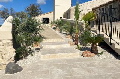 Terrasse en pierre avec piscine, chaises longues, parasols et bâtiments en pierre sous un ciel dégagé.