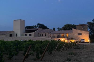 Terrasse en pierre avec piscine, chaises longues, parasols et bâtiments en pierre sous un ciel dégagé.