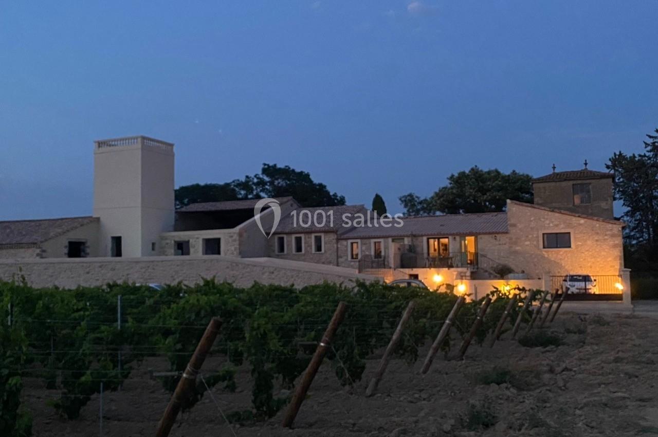 Bâtiment en pierre éclairé à la tombée de la nuit, entouré de vignes et d'arbres.