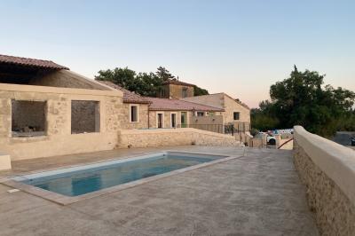 Terrasse en pierre avec piscine, chaises longues, parasols et bâtiments en pierre sous un ciel dégagé.