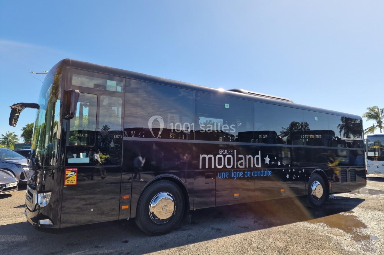 Autocar noir stationné sur un parking ensoleillé, avec le logo ’Groupe Mooland’ visible sur le flanc.
